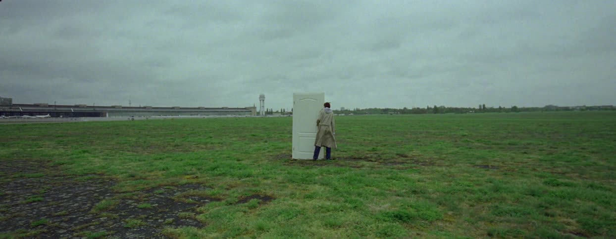 Person opens and walks through a door standing alone in a field near the airport on an overcast day