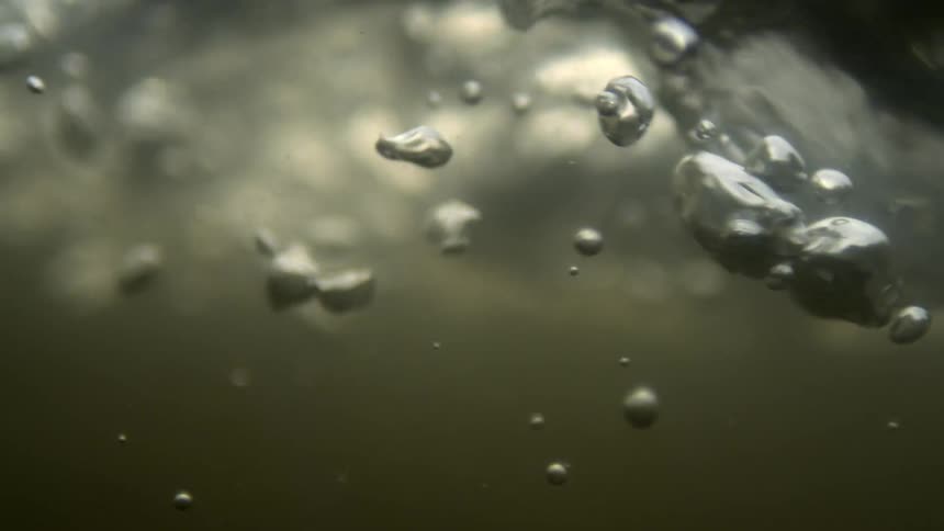An underwater view of a clear liquid with a partially greenish bottom and some bubbles moving to the right side