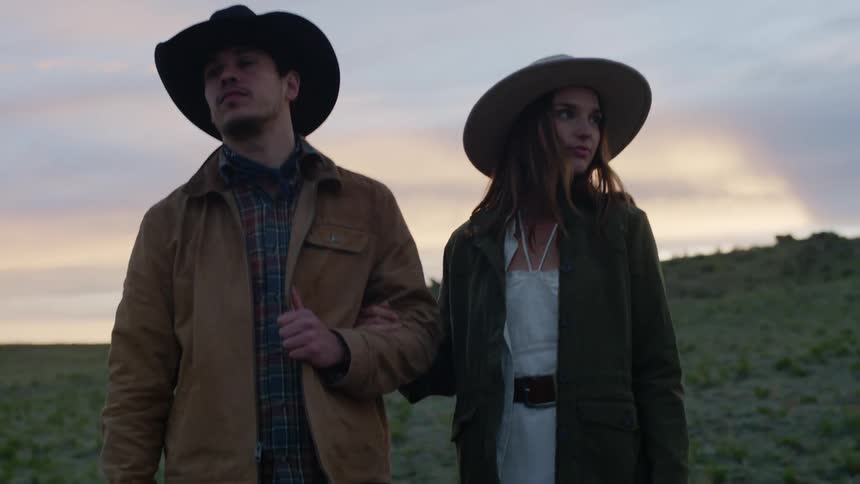 Couple with arms together both wearing hats walking down a hill in the late afternoon