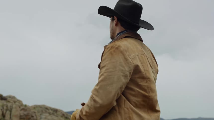 Cowboy in hat climbing on top of a rock on a hill on a cloudy day
