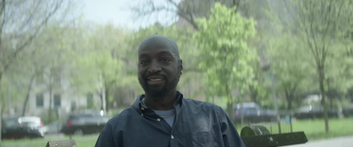 A man wearing a blue shirt sits on a park bench