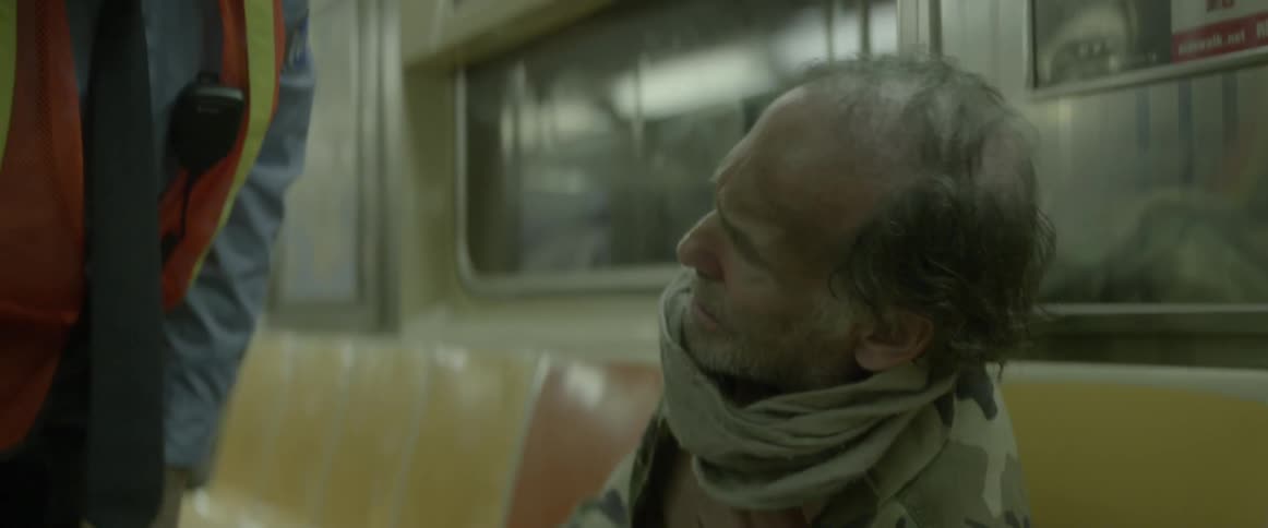 A worker shakes a homeless man awake on a train