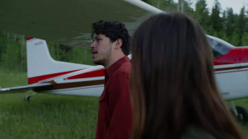 Man and woman walk by a small airplane sitting outside a forest