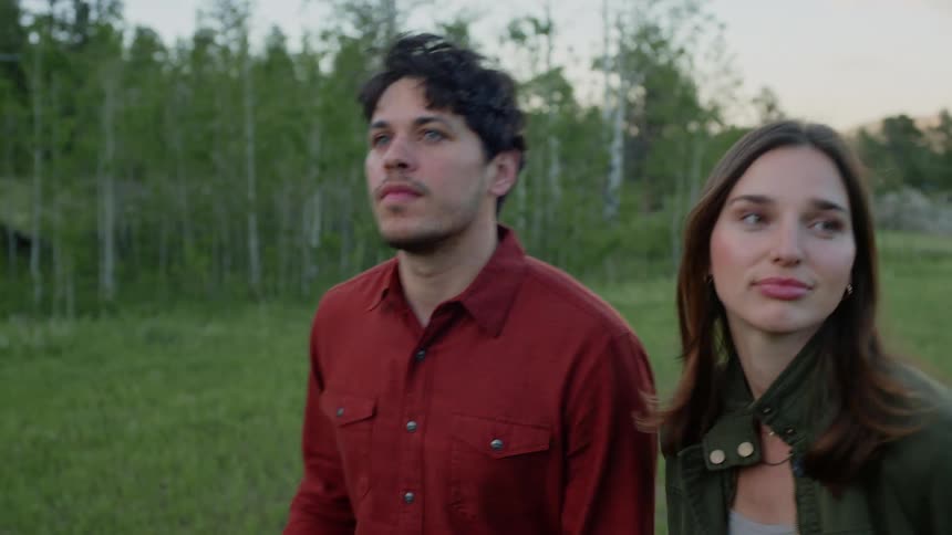 A man and a woman are walking on a green incense and they are talking and the man is holding a cowboy hat