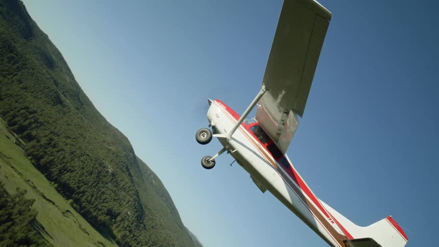 A small airplane flying over a lush green landscape with mountains in the background