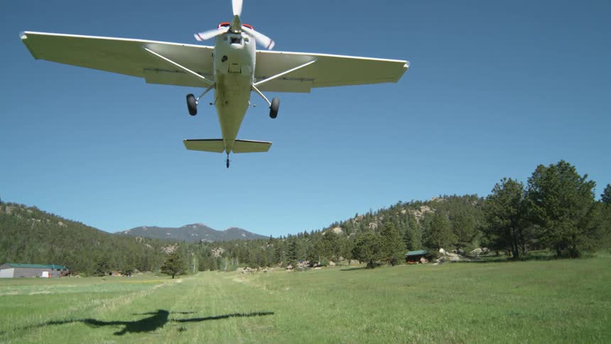 Small private plane taking off in a field with forests and mountains in the background