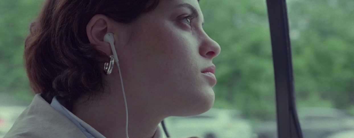 A woman rides through a city in the backseat of a car while listening to ear buds