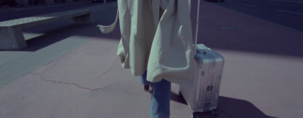 A person walking away pulling a silver suitcase with their coat flowing behind them