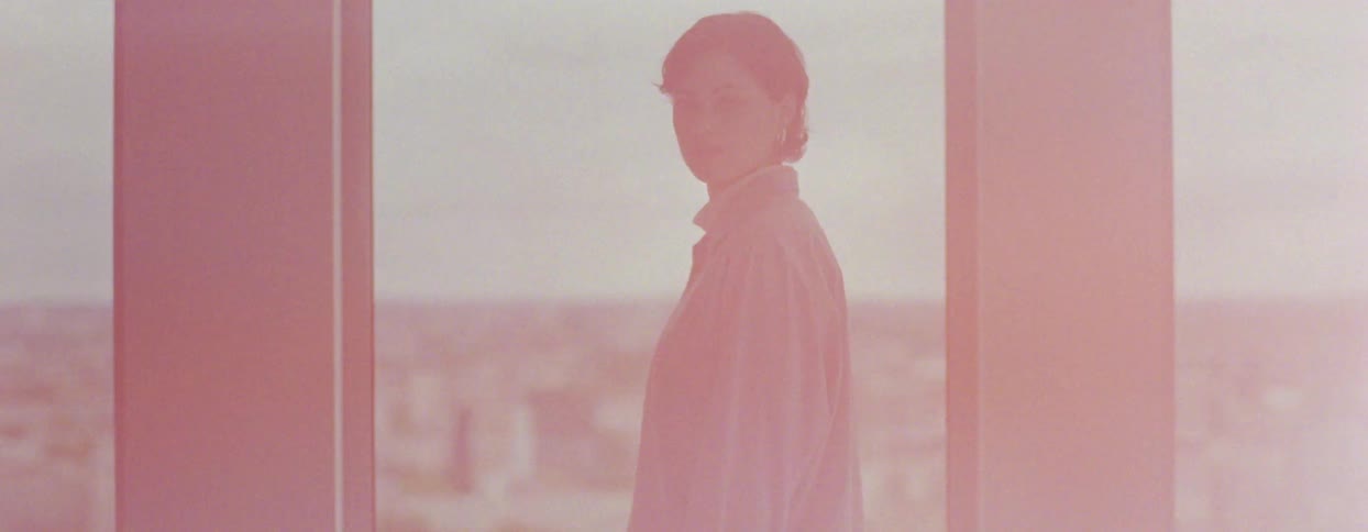 A woman stands at a glass window and turns around as bright lights flash
