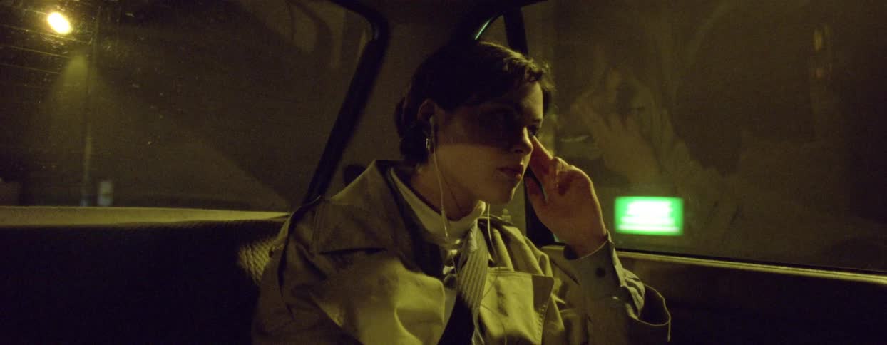 A young woman sitting in the back seat of a car and she is wearing headphones and then she looks out the back window