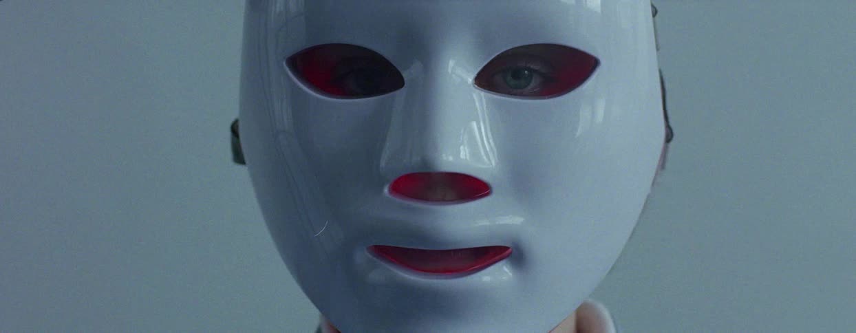 A person wearing a white light therapy face mask with red light glowing