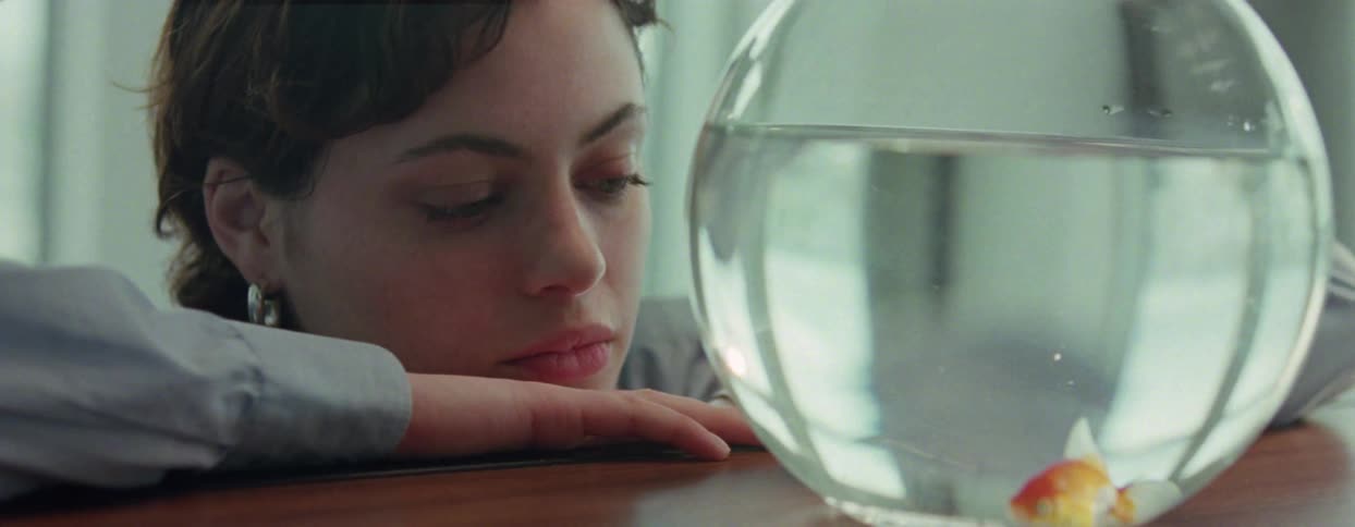 Young woman watching a small goldfish in an aquarium on a table