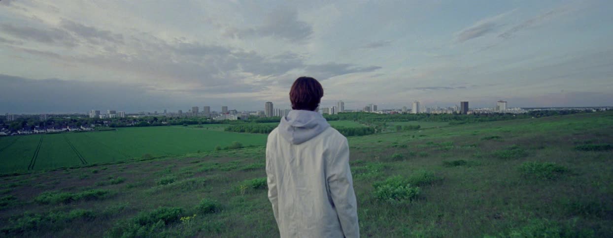 Woman with her back turned in a vast field with a metropolis on the horizon