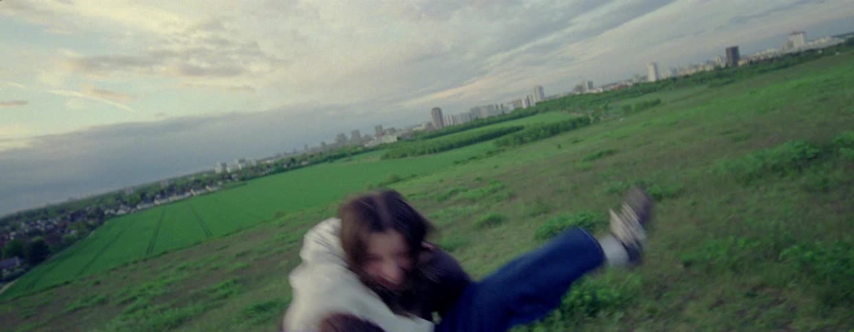 Two friends in a field picking each other up and falling to the ground while playing