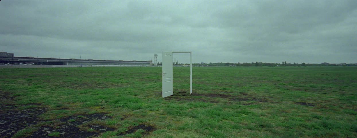 An open door stands alone in a field on a stormy day