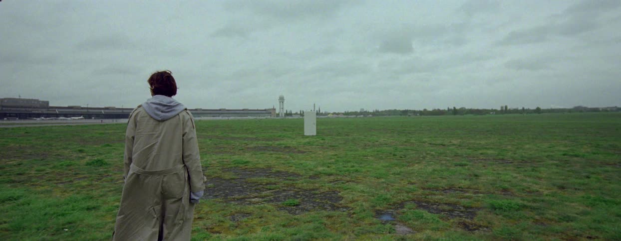 Field with basque grass and a woman walking towards a door in the middle