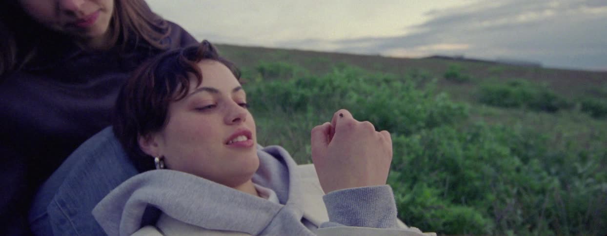 A young woman admires a beetle on her hand while she leans against her friends legs