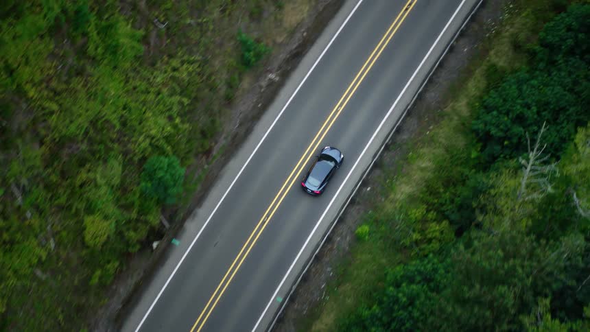 Aerial view of a black vehicle traveling on a highway surrounded by trees