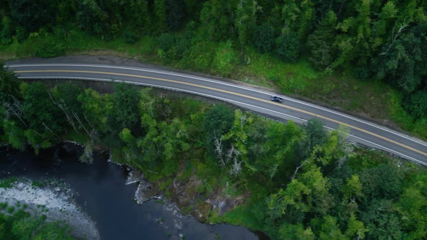 Car drives along a highway paralleling the river while it passes through a forest