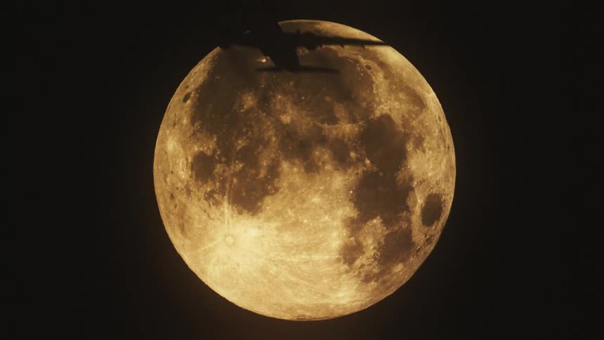 A passenger plane flies in front of a brightly lit moon