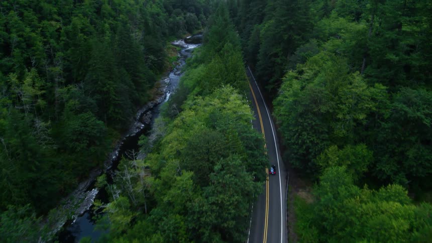 An aerial view of a car driving down a winding road surrounded by lush green forests and a river
