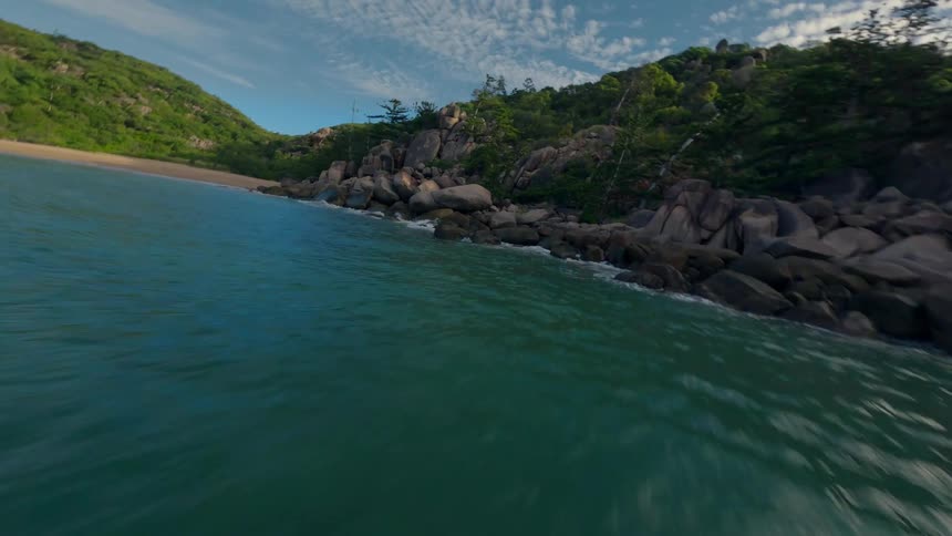 A deserted bay beach with rocks to one side and a grassy hill to the other
