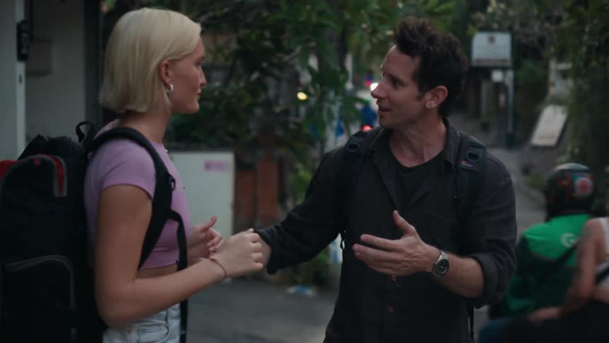 A man and a woman talk and hug while standing near a city street