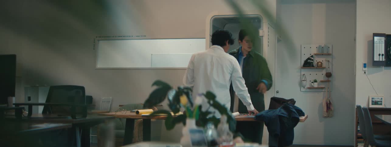 Woman with a prosthetic hand picks up and gives a binder to a man while they stand in an office