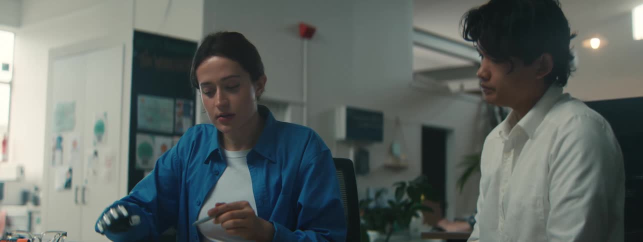 Woman with a robotic hand working at a desk next to a colleague