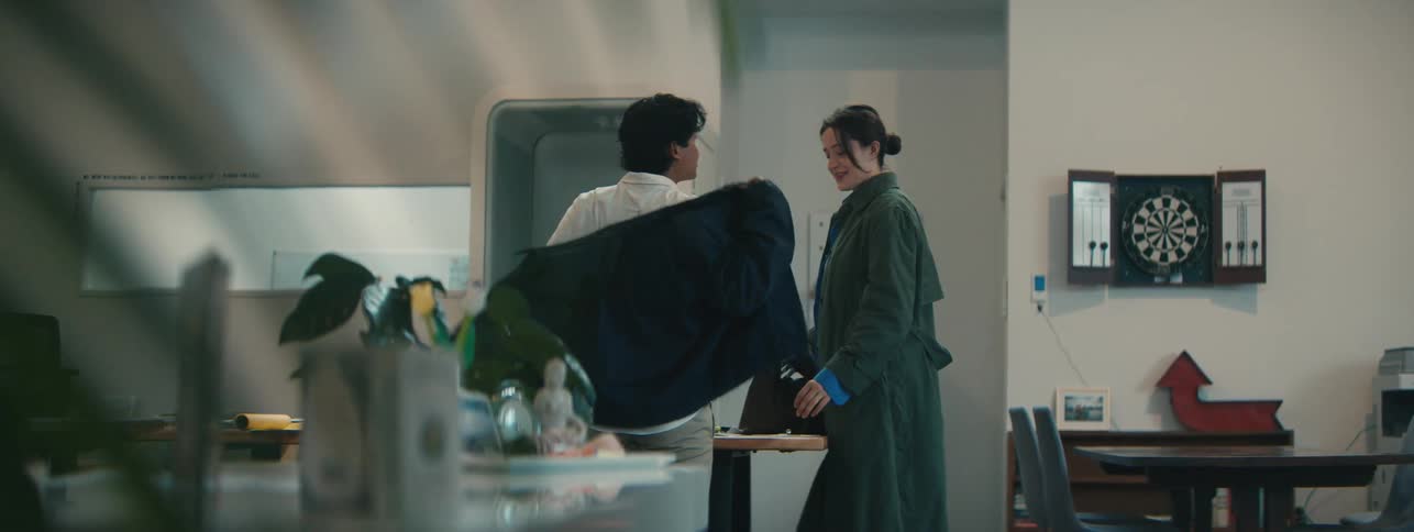 Woman and man in an indoor environment leaving their bag on a table and taking off their coat while talking