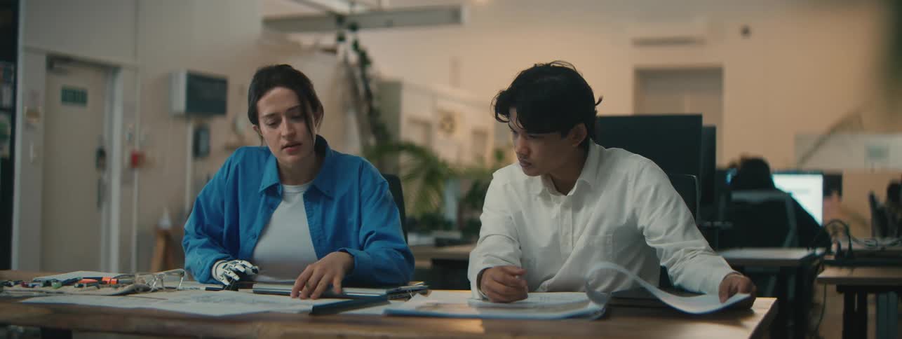 Man sitting next to a woman with a robotic arm talking at a table