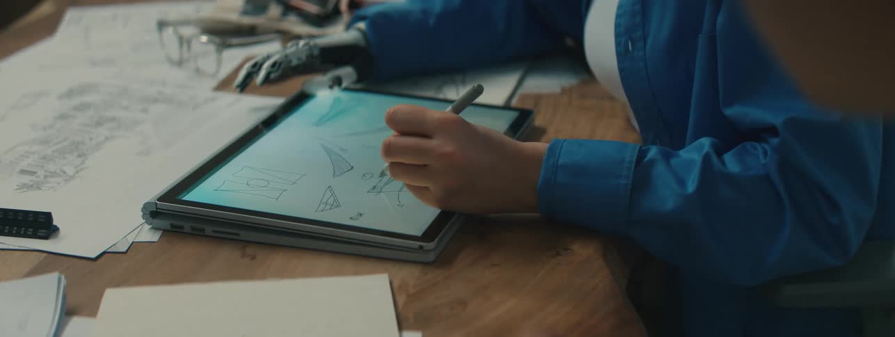 A woman with a prosthetic right hand draws on a tablet with her left hand