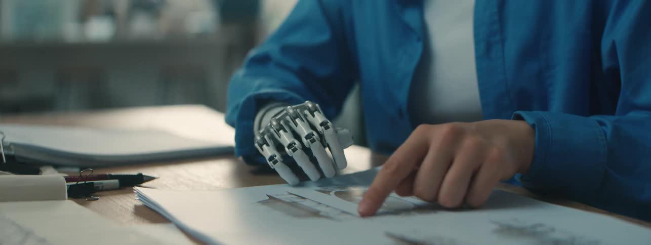 Close up of a womans hand with a robotic arm turning the page of a book
