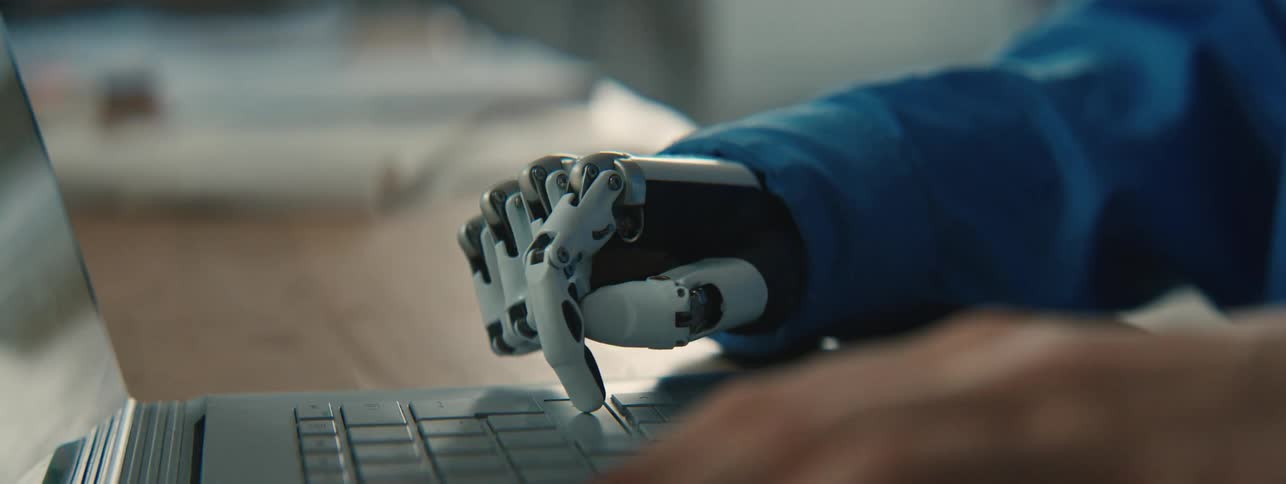 A woman with a prosthetic hand types on a laptop
