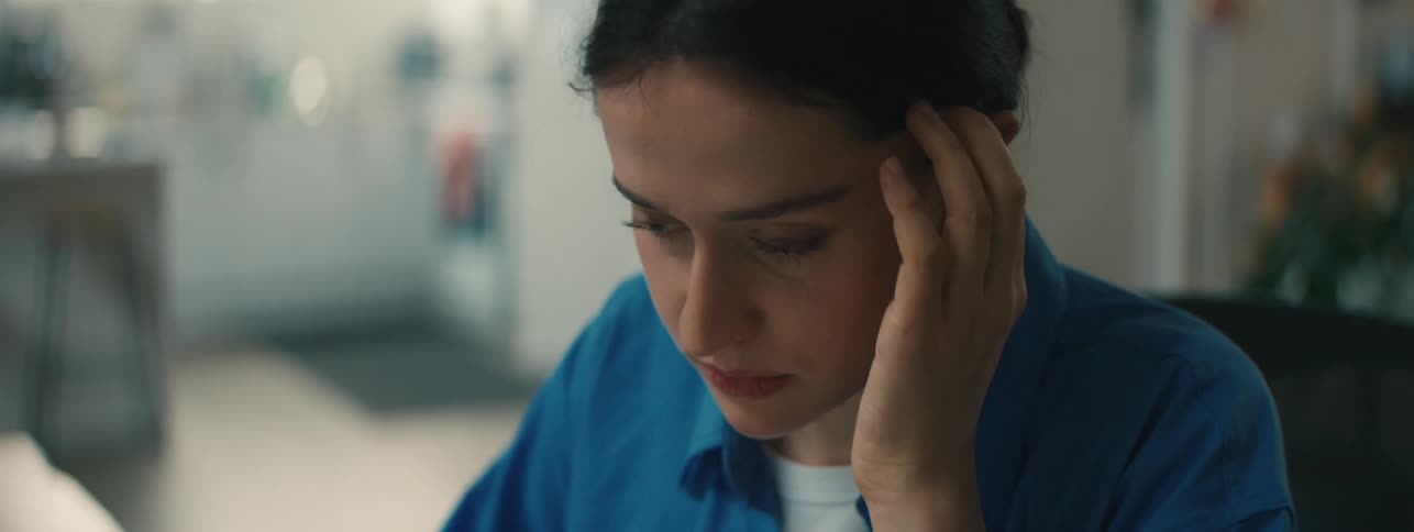A contemplative woman touches her face and adjusts a strand of hair behind her ear