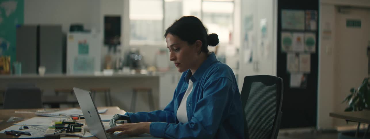 Office worker with a prosthetic hand sits down at a table with a laptop