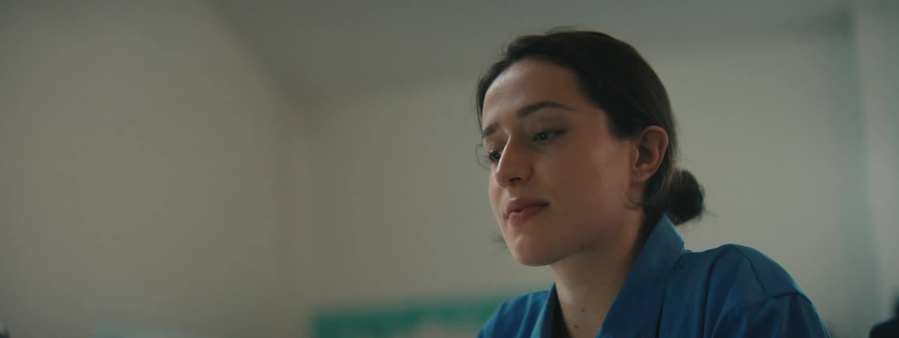 Close up of the face of a woman wearing a blue top sitting on a room lost in thought