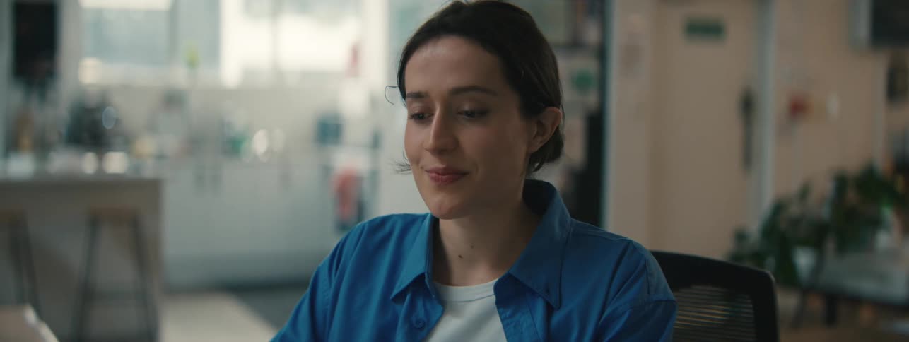 A woman sitting in a desk chair smiles to herself