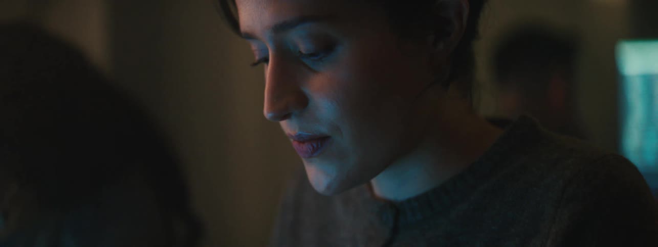 A woman with a sad expression staring at a computer screen the light from which shines on her face