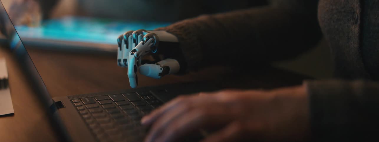 A person is typing on a laptop with a prosthetic limb