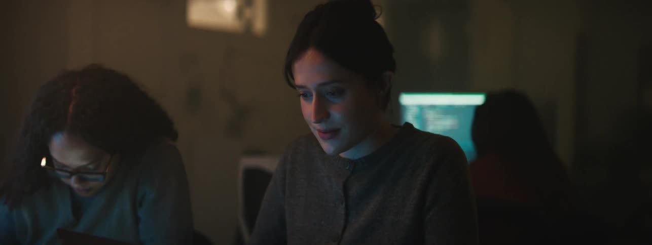 A woman in a room with two other women lets out a frustrated sigh while working on a computer