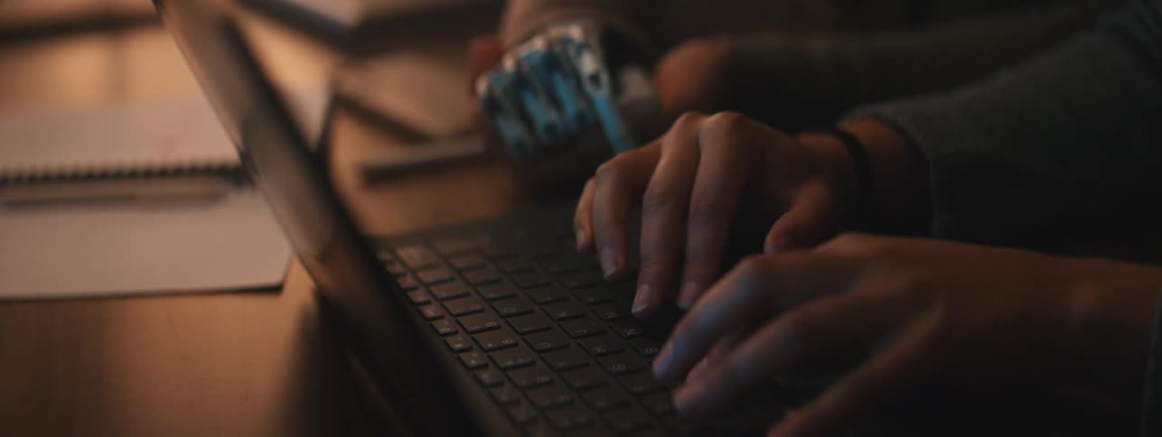 Two women sit at a table while one types furiously on a keyboard
