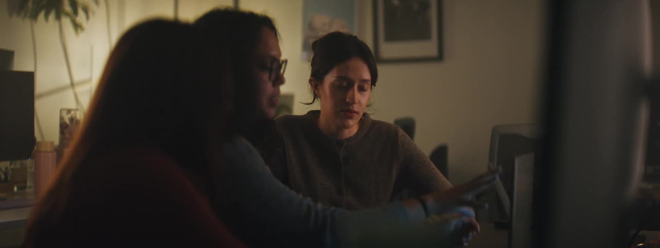 Three young women sitting at a table in front of a laptop talking