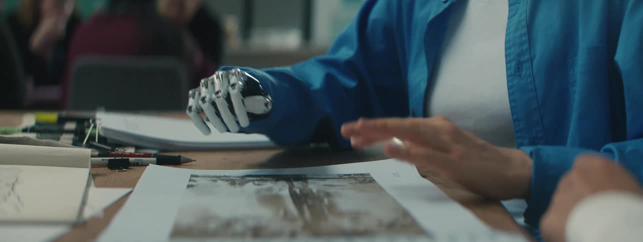A woman with a prosthetic hand works with a man at a table filled with photographs