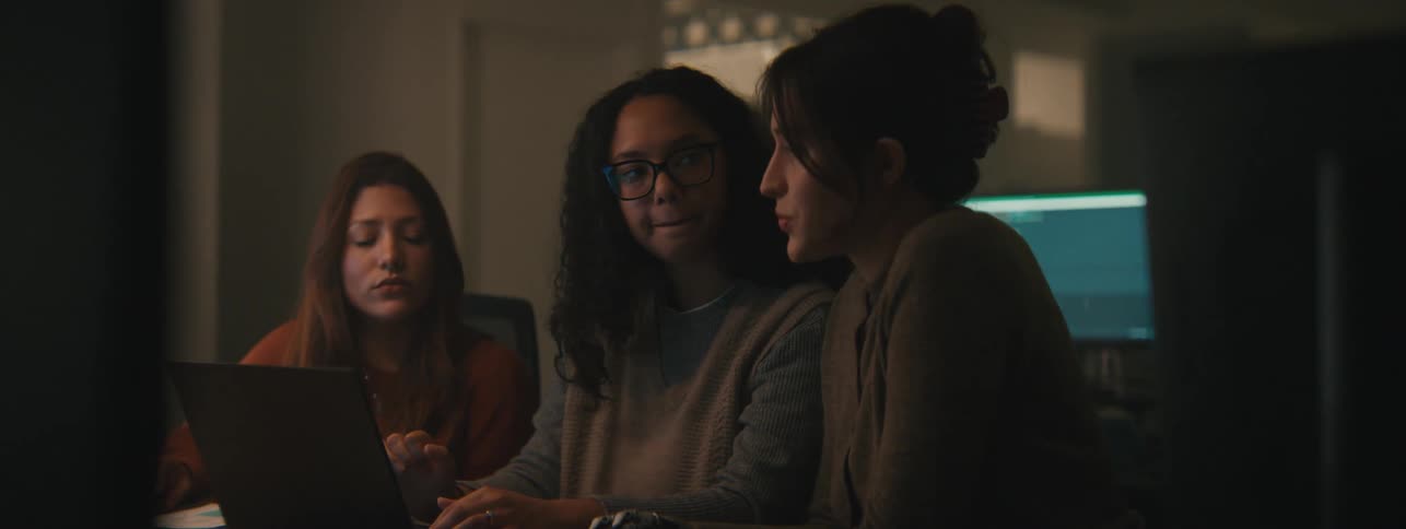 Three women collaborating intently around a laptop in a dimly lit environment