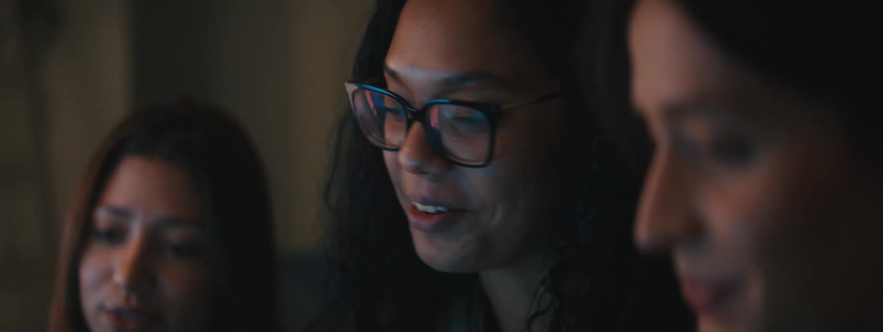 Three women engaged in conversation with one woman smiling and wearing glasses