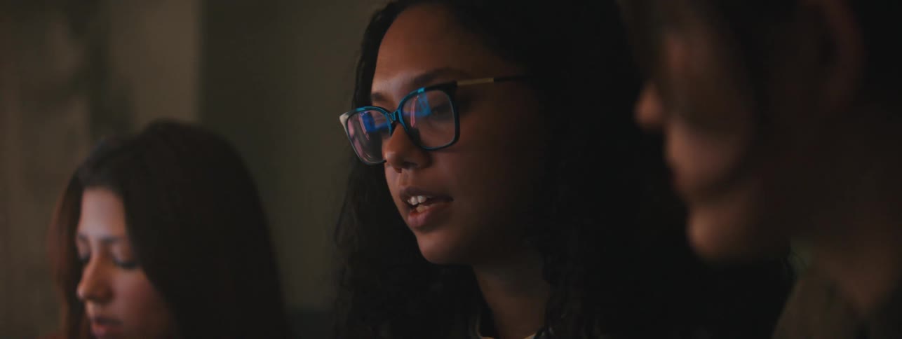 Three women engaged in conversation with one woman wearing glasses and speaking intently