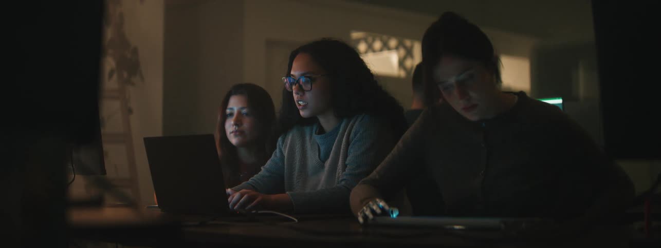 Three women are using devices and talking
