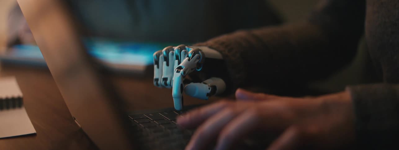 Robotic hand and human hand typing on a laptop