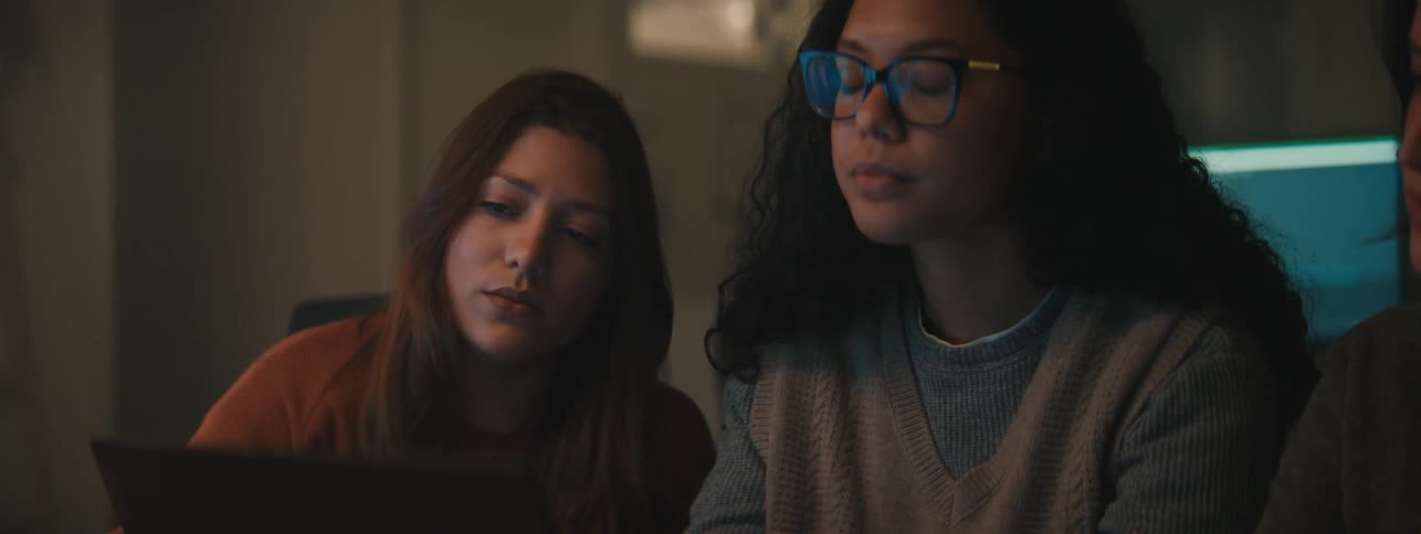 Three young women sit together at a laptop and talk about what is on the screen